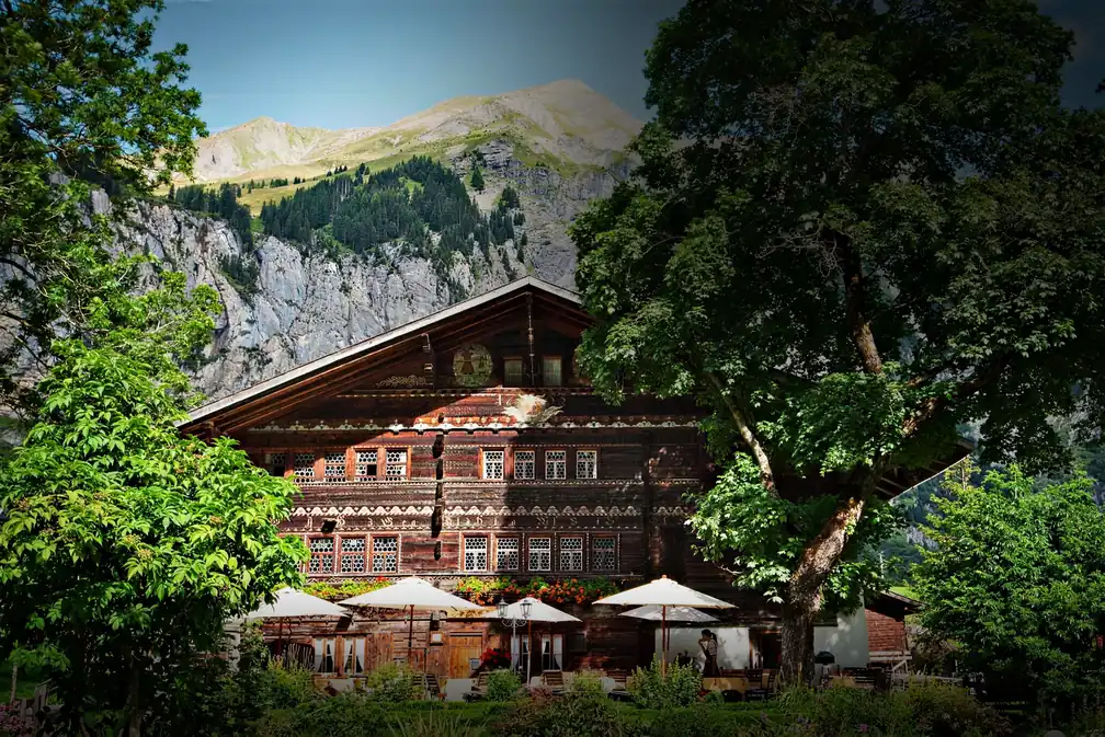 Das Haus im Sommer mit Sonnenschirmen im Garten, dahinter Fels und Gipfel